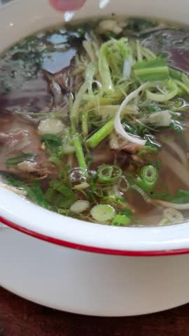 Experience authentic Vietnamese Pho, a rich, flavorful noodle soup. Witness the careful arrangement of fresh herbs and vegetables, enriching the savory broth and creating an aromatic flavor.