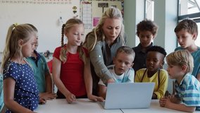 Teacher tapping laptop screen and guiding children at classroom table, illustrating network icons. Education, digital learning, creativity, collaboration, technology, classroom, innovation - Powered by Shutterstock - Get 15% off with code: PIKWIZARD15