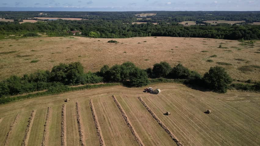 Tractor harvesting grass and making hay bales in field, aerial drone view. Aerial drone footage of a tractor working in an agricultural field during summer. The machine harvests grass and packs it 