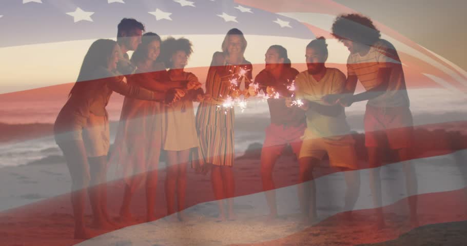 Group of eight adults igniting sparklers on dusk shoreline for holiday marketing with animated flag. Celebration, camaraderie, twinkle, sunset, festivity, unity, leisure