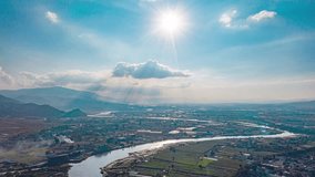 Aerial view of Ruili border region between China and Myanmar, showing winding river, agricultural land, mountains, and dramatic sky with sunbeams breaking through clouds. - Powered by Shutterstock - Get 15% off with code: PIKWIZARD15