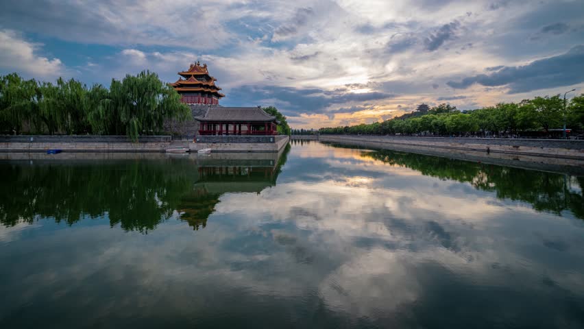 Ancient Chinese pagoda tower reflected in moat waters at Forbidden City corner, Beijing. Traditional architecture with dramatic sky and perfect water reflection at sunset.