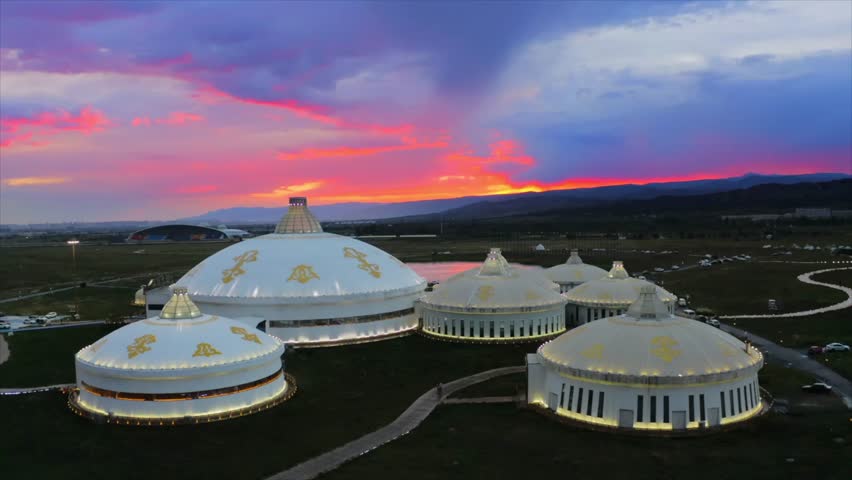 Aerial view of traditional Mongolian yurt-style architecture illuminated at sunset over grassland landscape with dramatic colorful sky in Mongolia