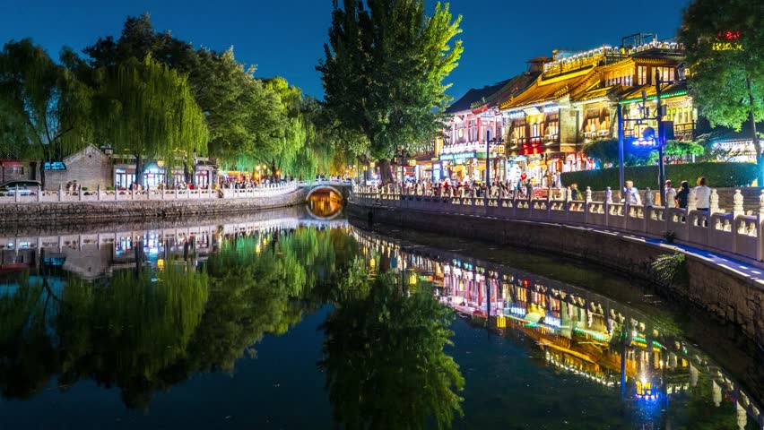Night view of illuminated traditional buildings and willow trees reflected in Qianhai Lake at Shichahai historic district, Beijing, China with vibrant evening lights