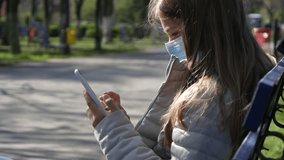 Sick Kid with Protection Mask Playing on Smartphone, Sad Child Using Smart Phone on Bench in Park, Girl in Coronavirus Pandemic - Powered by Shutterstock - Get 15% off with code: PIKWIZARD15