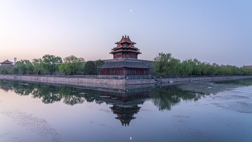 Ancient Chinese tower and architecture reflected in water at Beijing Forbidden City during twilight with crescent moon visible in purple sky
