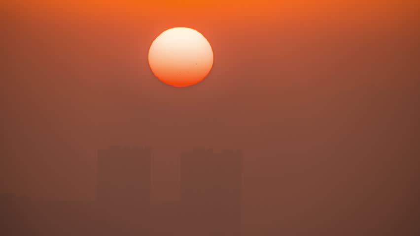 Stunning large orange sun setting against warm gradient sky with beautiful atmospheric haze and soft lighting effects captured in ultra high definition timelapse footage.