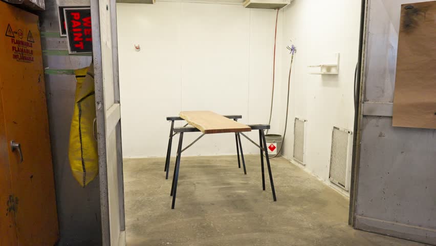 Slow motion push in on raw wood slab on riser inside paint spray booth