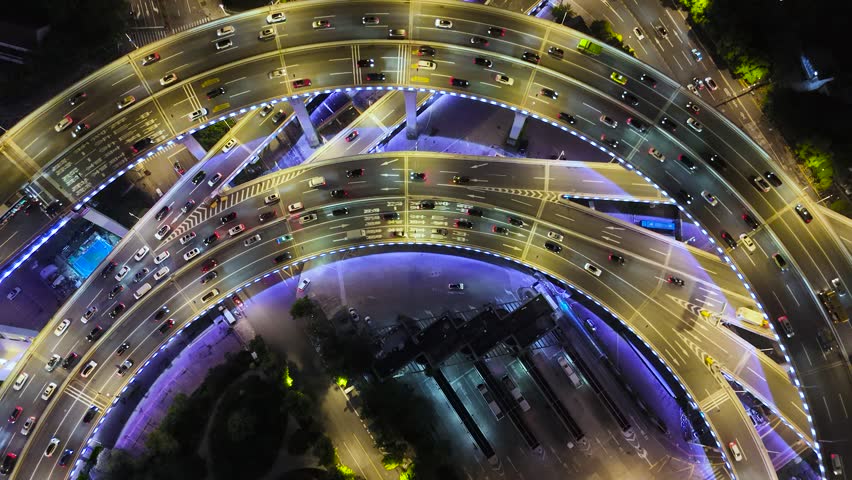 Aerial view of a complex highway interchange illuminated at night, with multiple lanes and moving cars in Shanghai.
