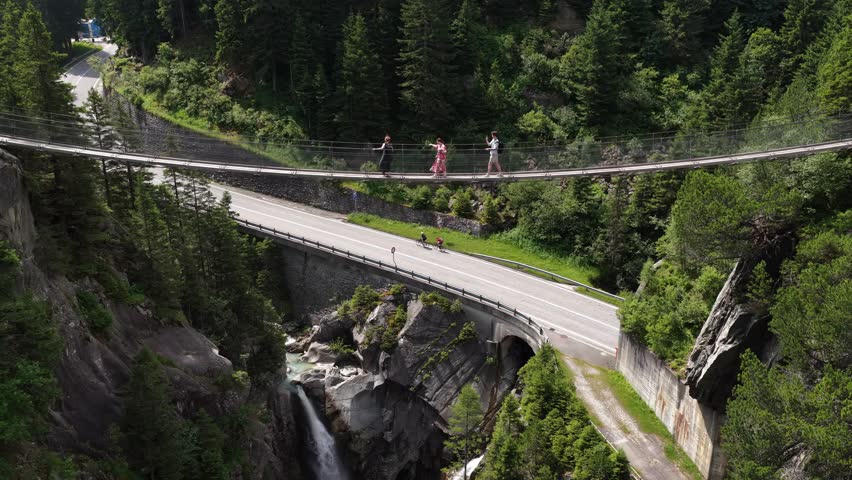 People walking on a suspension bridge over a mountain gorge and waterfall, Switzerland