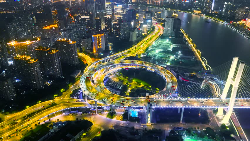 Aerial of the illuminated Nanpu Bridge interchange with heavy night traffic, surrounded by high-rise buildings and the Huangpu River, Shanghai, China.