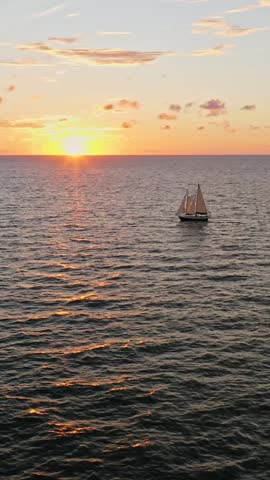 A lone sailboat moves gracefully across the ocean as the sun sets, scattering golden reflections across rippling waves beneath a sky painted with warm evening tones.