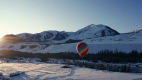 Colorful hot air balloon floating over snowy winter landscape with mountains and forest at golden hour sunset, creating a breathtaking aerial adventure scene. - Powered by Shutterstock - Get 15% off with code: PIKWIZARD15