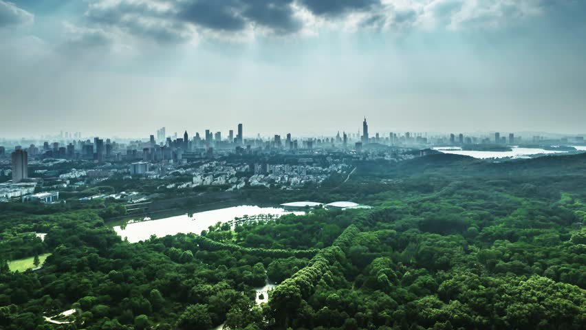 Aerial panoramic view of Nanjing city skyline with Zhongshan botanical garden in foreground, dramatic cloudy sky and urban landscape stretching to horizon