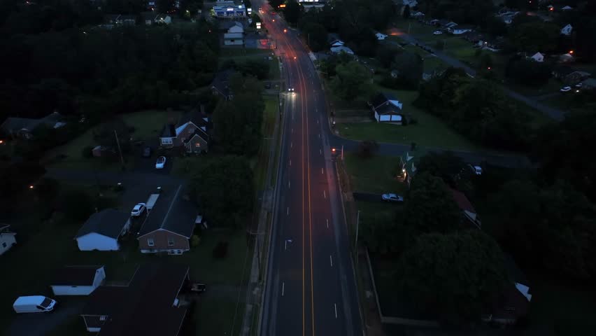 Traffic on suburb road at dusk. American neighborhood with lighting lantern on rainy day on USA. Aerial Birds Eye shot. Cars on intersection street in suburbia.