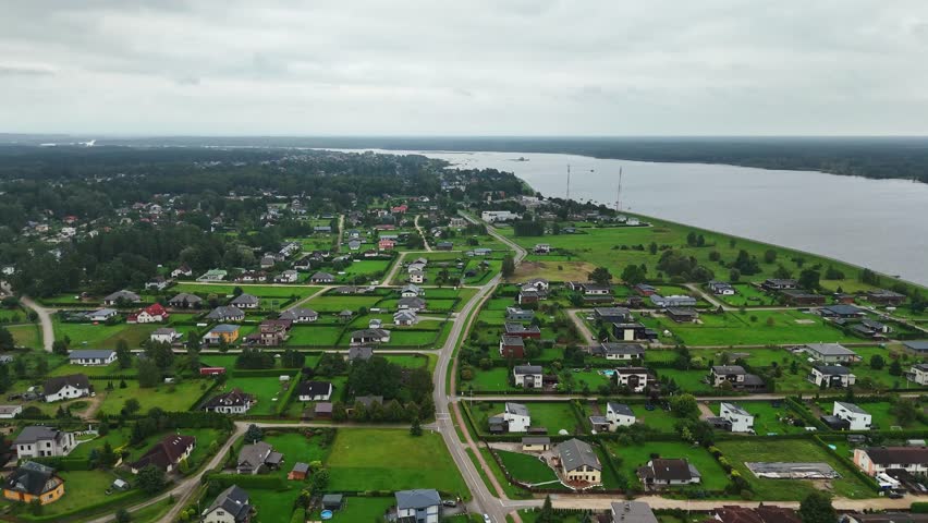 Residential terrain of Ikskile, revealing housing terrain near the Daugava River with green plots calm water and road layout, located in Ogre Municipality, part of the Zemgale Region of Latvia.