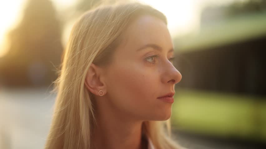 Smiling blonde woman outdoors at sunset, looking happy and confident with warm golden light creating soft bokeh background