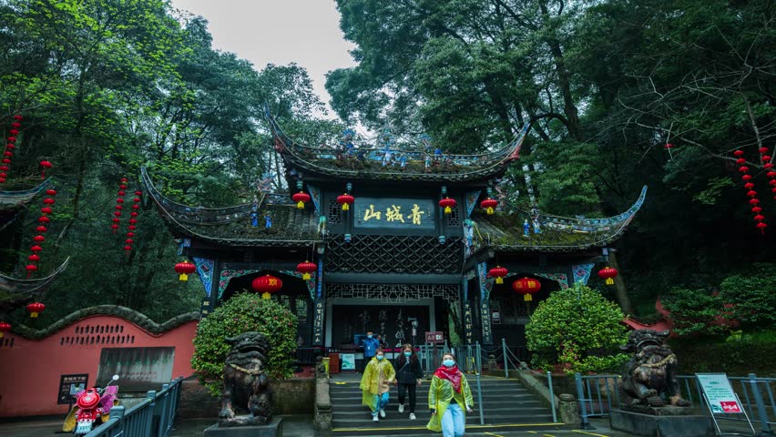 Traditional Chinese temple entrance at Qingcheng Mountain near Chengdu, featuring ornate architecture with red lanterns, curved roofs, and stone lion guardians amid lush greenery.