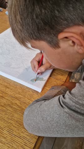 Young boy painting a canvas at home using thick tempera paints and a paint-by-numbers guide in a calm, focused atmosphere