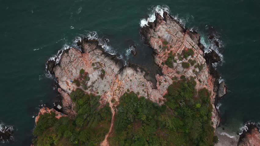 An aerial view over the rocks and rocky shores of Fort Wetherill State Park in Jamestown, Rhode Island during a cloudy day. The drone camera is tilted downward and is stationary.