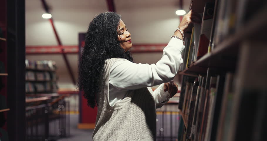 Smile, woman and search for book in library for author choice, research and information on art. Mature teacher, night and reading title of novel for learning, lecture preparation and course knowledge