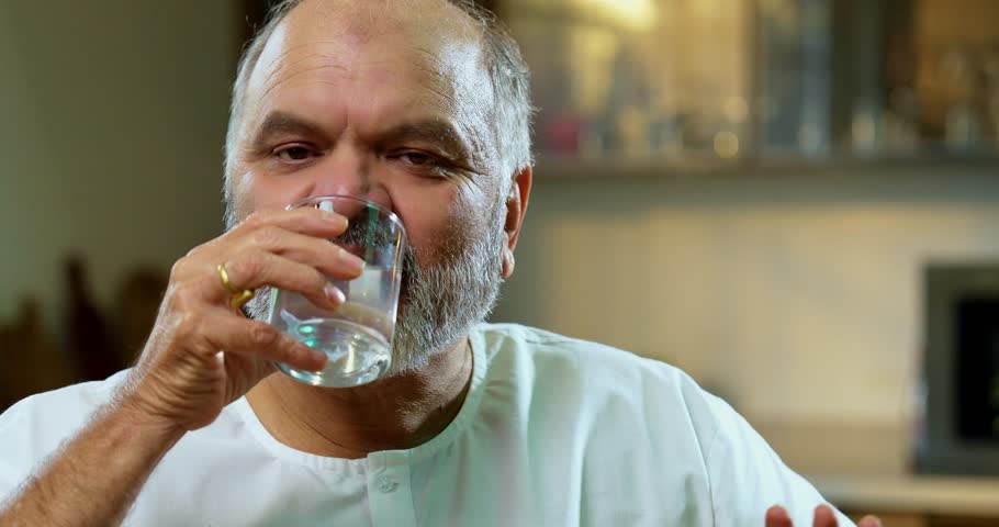 Senior Indian man drinking coconut water directly from green coconut in modern kitchen, Asian elderly person enjoying natural tropical drink for hydration, health, nutrition, and summer refreshment