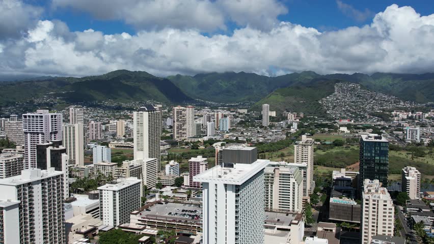 Stunning 360 aerial drone view of Honolulu, Hawaii, showcasing the tropical city skyline, turquoise Pacific Ocean, beaches, and lush mountains in the distance. Perfect for travel and tourism footage.
