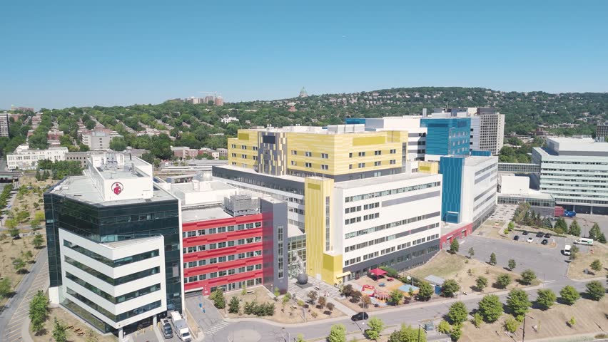 Aerial view of MUHC hospital complex in Montreal, featuring Shriners Hospital and Montreal Children’s Hospital, modern medical architecture. Mount Royal in background.