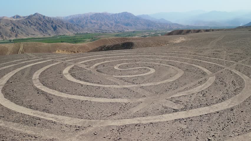 Aerial parallax shot of the spiral geoglyph among the Nazca Lines etched in the arid desert of southern Peru with mountain backdrop