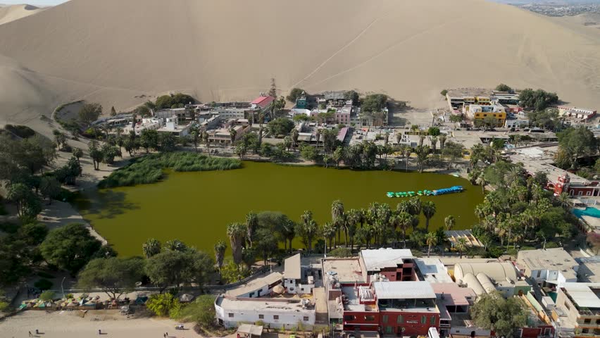 Stunning aerial reveal shot of the Huacachina village and lagoon a lush desert oasis surrounded by massive sand dunes in Ica Peru