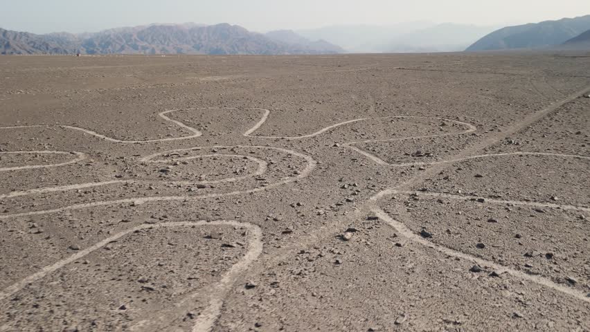 Aerial parallax shot moving over the intricate flower-shaped Nazca Lines geoglyph in the desert plains of Peru, an ancient UNESCO World Heritage Site featuring enigmatic lines and barren landscapes