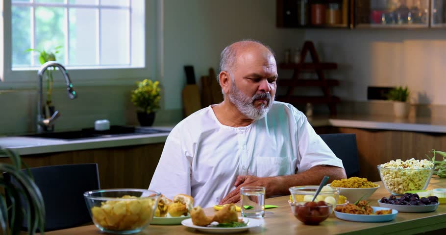 Senior Indian man drinking antacid in modern kitchen, Asian elderly person experiencing acidity or indigestion after food, taking antacid liquid to ease discomfort and feel better at home