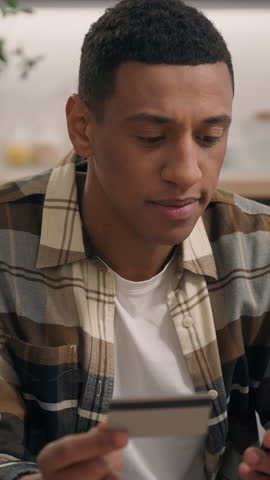 Confused anxiety African American man shopping online with mobile phone and bank credit card worried buyer guy male e-commerce trouble ordering delivery internet store buying failure pondering problem