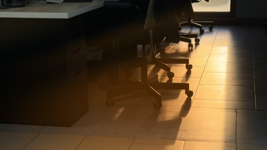 Empty office chairs and desks with morning sunlight casting long shadows on the floor. Perfect for business, workplace, lifestyle, and cinematic projects.