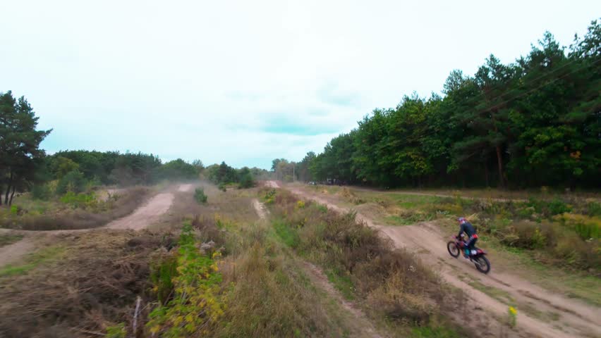 Exciting FPV drone chase of two motocross riders competing on a forest dirt track. Riders jump ramps, race at high speed, and showcase extreme motocross action from a cinematic aerial perspective.