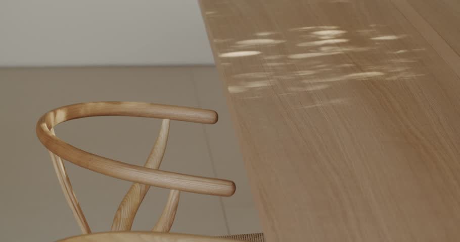 Sunlight streams onto a wooden dining table, creating a warm, inviting atmosphere. A stylish wooden chair with a woven seat sits next to the table, ready for guests.