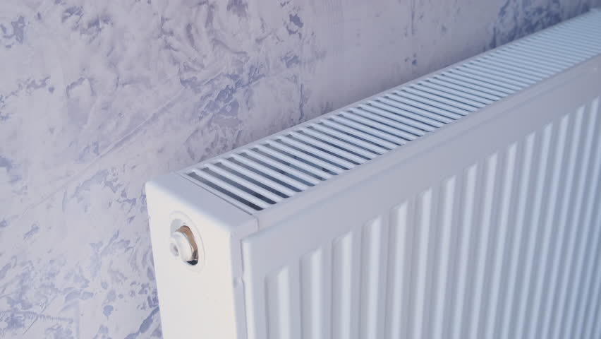 Closeup of man warming his hands in yellow sweater on the heater at home during cold winter days. Male getting warm up his arms over radiator. Concept of heating season or cold weather