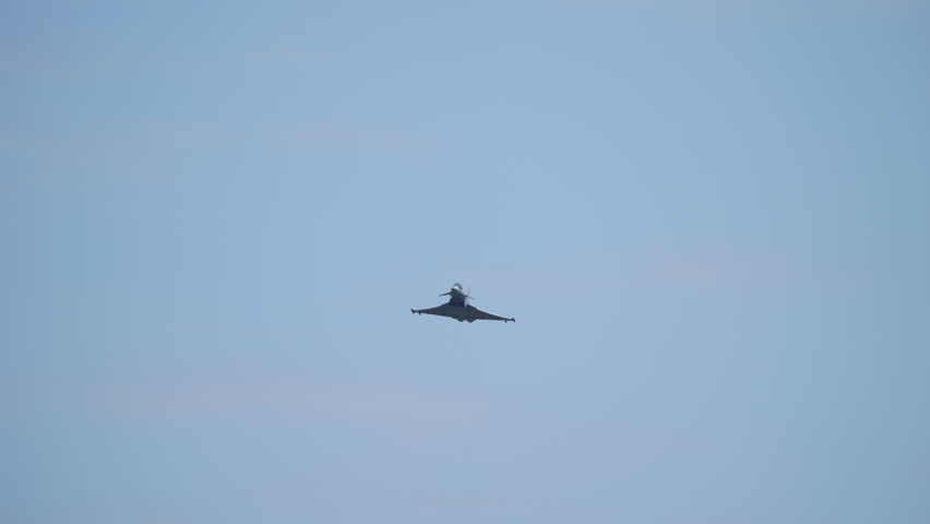 Military jet captured flying directly overhead in a slow motion sequence against blue sky