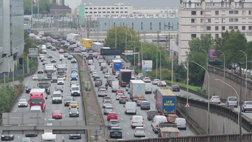 Aerial 4K drone shot of dense traffic jam on the Paris ring road with cars, trucks, and urban infrastructure during rush hour.
