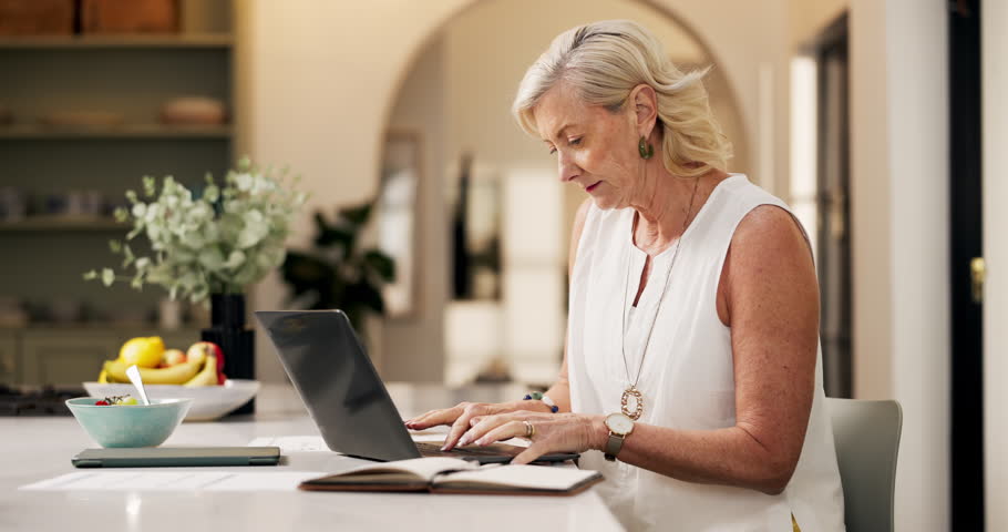 Typing, paper or mature woman in home with laptop, online research or editing of blog post. Reading, WFH or journalist in kitchen with technology, information gathering or source feedback for article