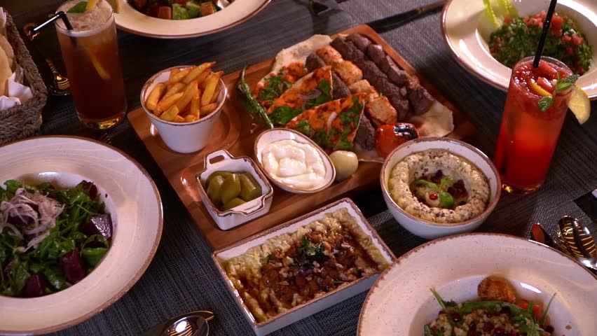 A beautifully arranged table with a variety of Middle Eastern dishes including salads, grilled meats, dips, and drinks.