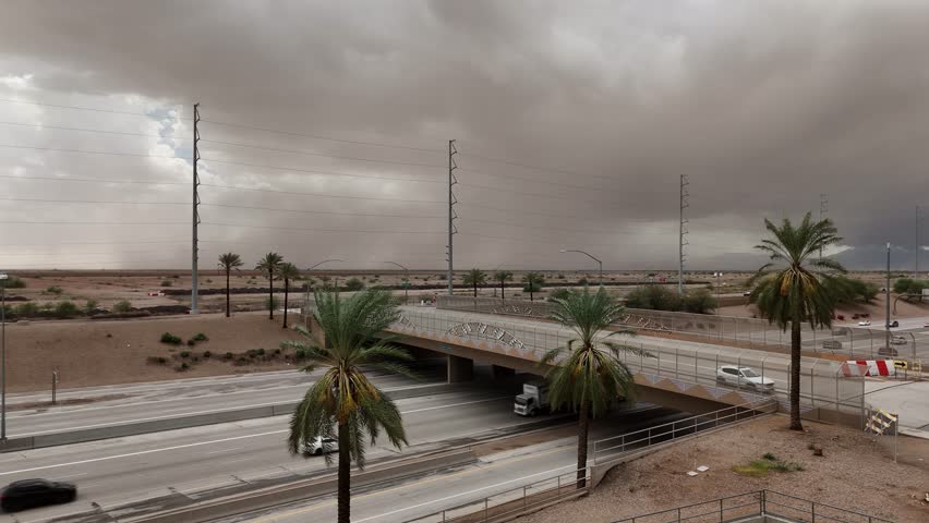 Static Shot of Highway 202 in chandler Arizona with Huge Dust Storm in the background, windy day, palm trees blowing in foreground, cars driving on highway