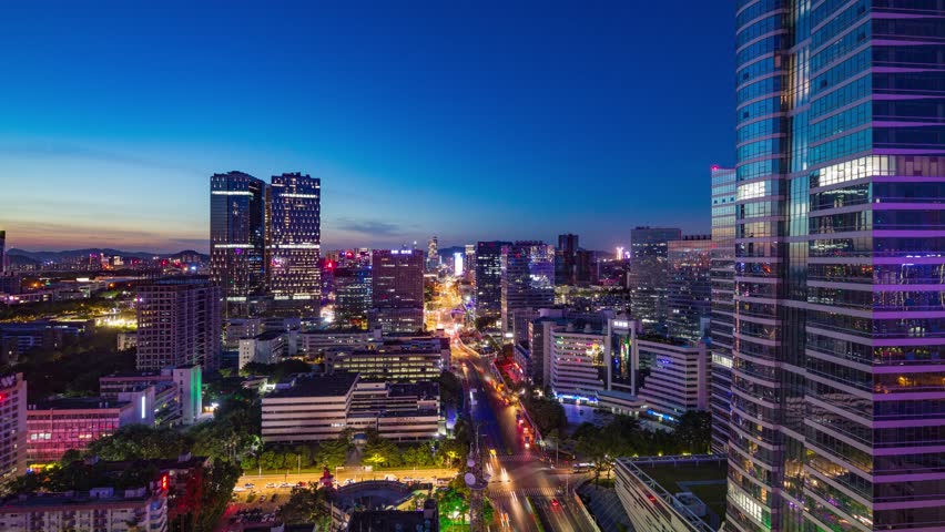 Night time lapse view of Shenzhen urban skyline with illuminated skyscrapers, light trails from traffic, and modern architecture in China
