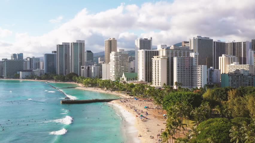 Aerial view of a coastal city skyline with high-rise buildings, sandy beach, and turquoise sea waves.