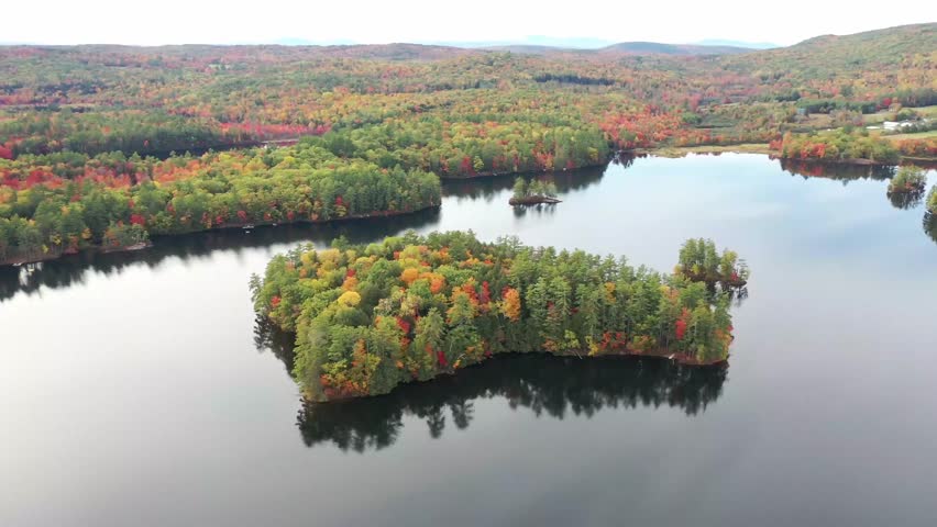 Aerial view of colorful autumn trees surrounding a calm reflective lake in serene nature.