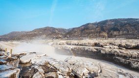 Time lapse view of frozen Hukou Waterfall with ice formations and mist creating rainbow effects against mountain backdrop in winter landscape - Powered by Shutterstock - Get 15% off with code: PIKWIZARD15
