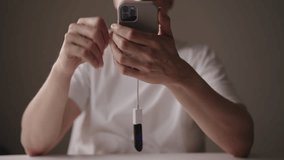 Portrait of young adult man using smartphone connected to OTG cable and adapter sitting at home office desk. Concept of data transfer or device connection. Shooting in slow motion. - Powered by Shutterstock - Get 15% off with code: PIKWIZARD15