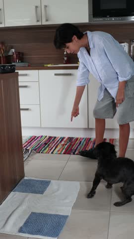 Young girl giving a bowl of food to a little black dog in a modern kitchen at home