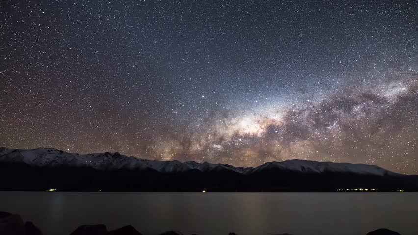 Stunning time lapse view of Milky Way galaxy stretching across starry night sky above snowy mountains and serene lake, creating magical astrophotography scene