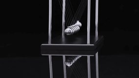 Newton's cradle pendulum demonstrating physics laws of motion and energy transfer with metal spheres suspended on strings in dark atmospheric lighting - Powered by Shutterstock - Get 15% off with code: PIKWIZARD15